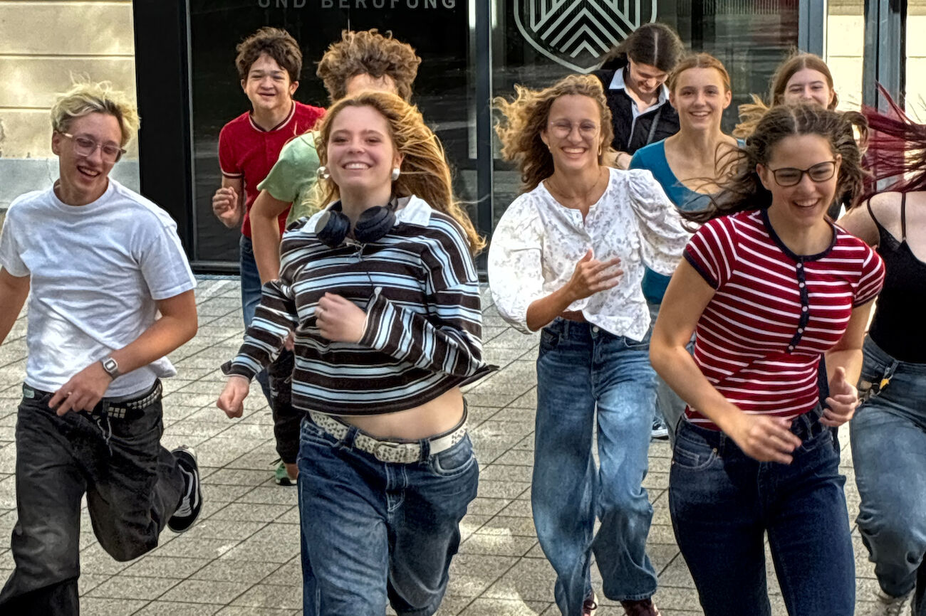 Sieben Teenager stehen im Kreis und halten jeweils Schnüre, die an einer hölzernen Nabe befestigt sind.